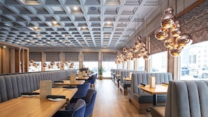 Een modern restaurantinterieur met houten tafels en grijze gestoffeerde zitbanken, met een patroonplafond en hangende sferische lampen.