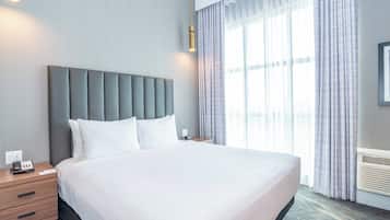A large bed with a grey upholstered headboard, white bedding, and a bedside table with a phone and a small item on it.