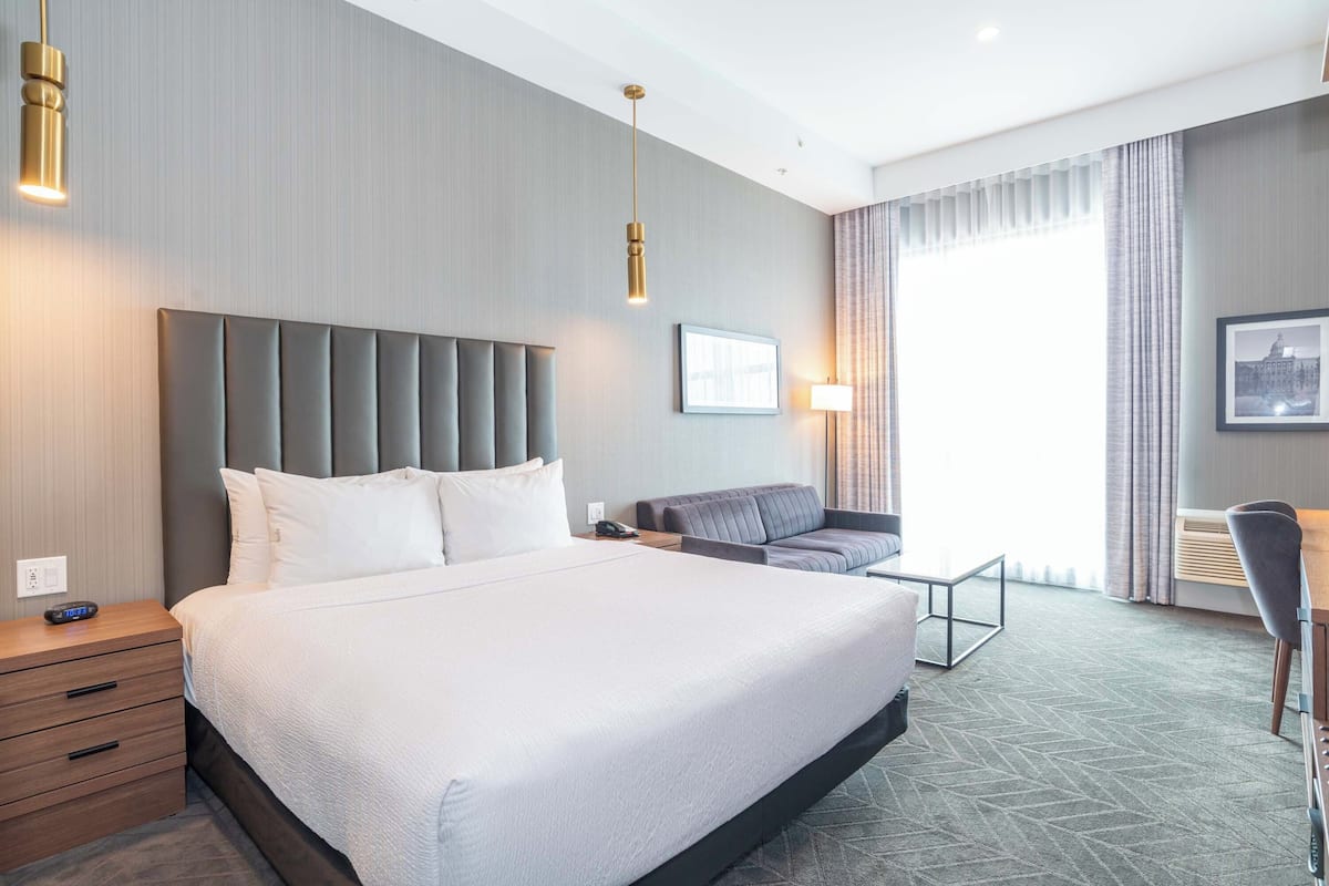 Een moderne hotelkamer met een groot bed, een bank, een bureau en uitzicht op de stad door het raam.