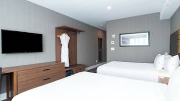 A modern hotel room with a flat-screen TV, a wooden dresser, a robe hanging, two beds, and a framed picture on the wall.