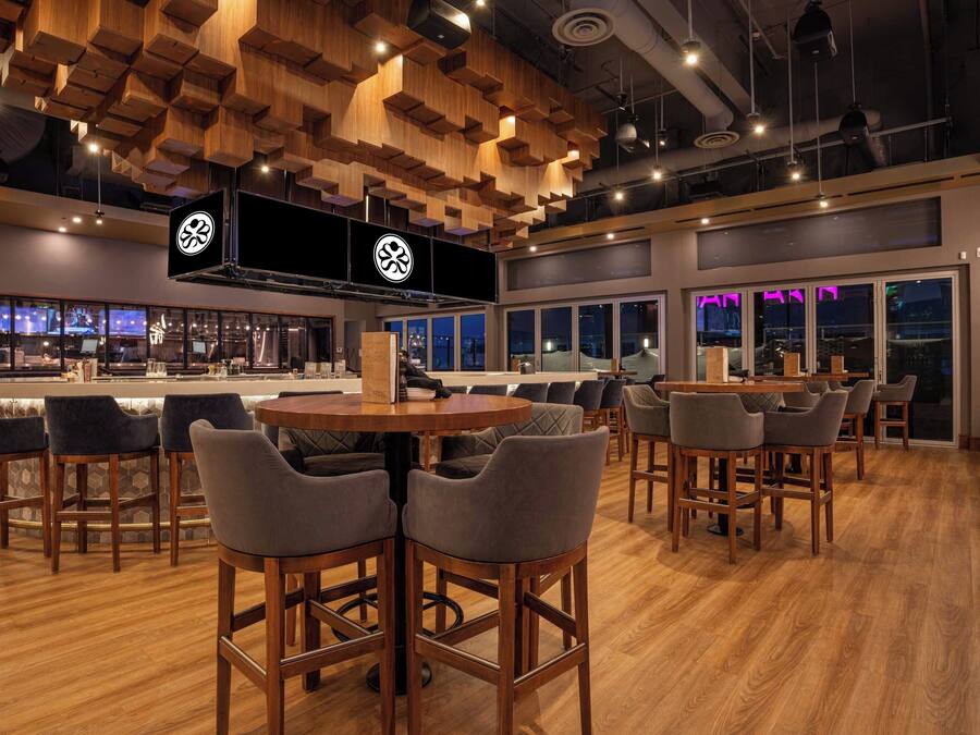 Un espace bar moderne, doté de mobilier en bois, d’un grand écran de télévision et offrant une vue sur la ville la nuit.