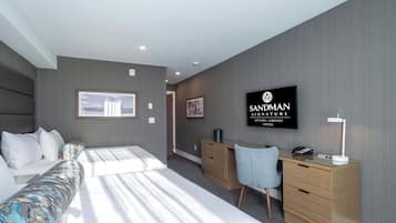 Habitación de hotel moderna con cama, escritorio, silla y televisión mostrando el nombre del hotel.