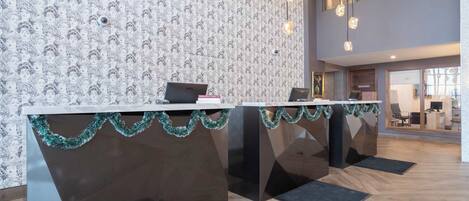 A reception desk with a patterned wallpaper, two laptops, and a modern chandelier.
