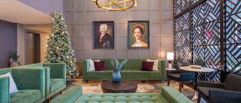 A lobby with a Christmas tree, green sofas, a round coffee table, and two framed portraits.