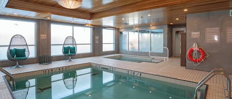 An indoor swimming pool with clear water, wooden ceiling, and seating areas with cushions.