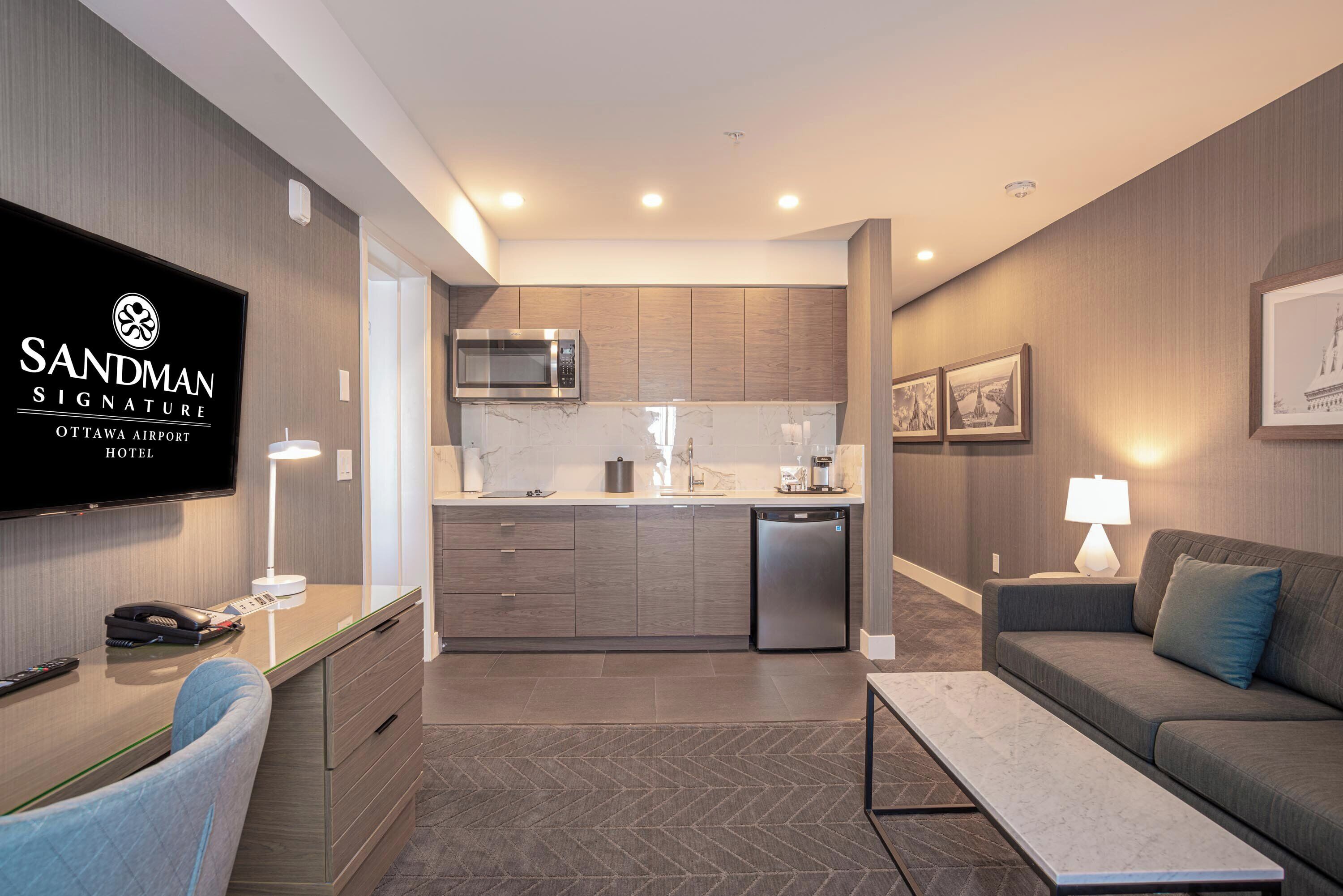 Una habitación de hotel moderna con cocina, sofá, televisión y escritorio.