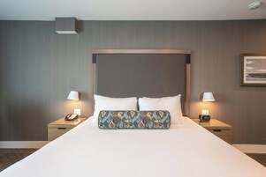 Una habitación de hotel con una cama grande, dos mesitas de noche, una mesita de noche con lámpara y un cuadro colgado en la pared.