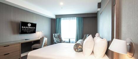Una habitación de hotel con cama, escritorio, sillas, televisor y ventana con cortinas.