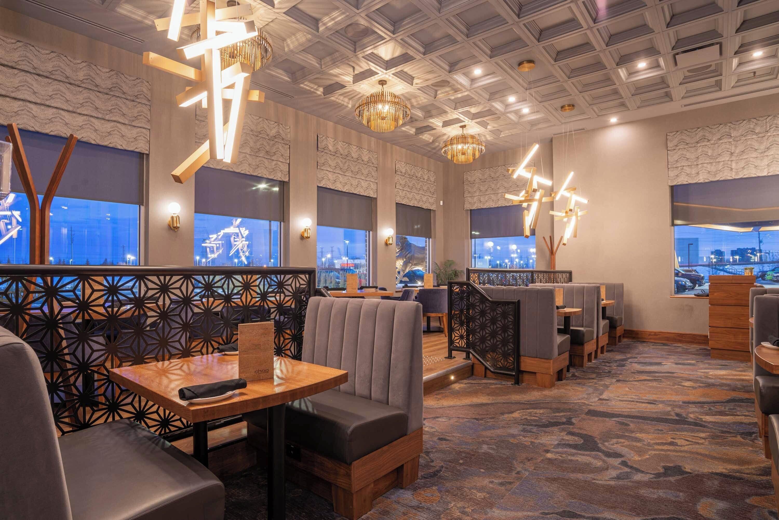 A modern restaurant interior with high ceilings, geometric wall patterns, and contemporary lighting fixtures.