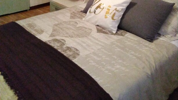Een slaapkamer met een bed, kussens, een nachtkastje en een kast.