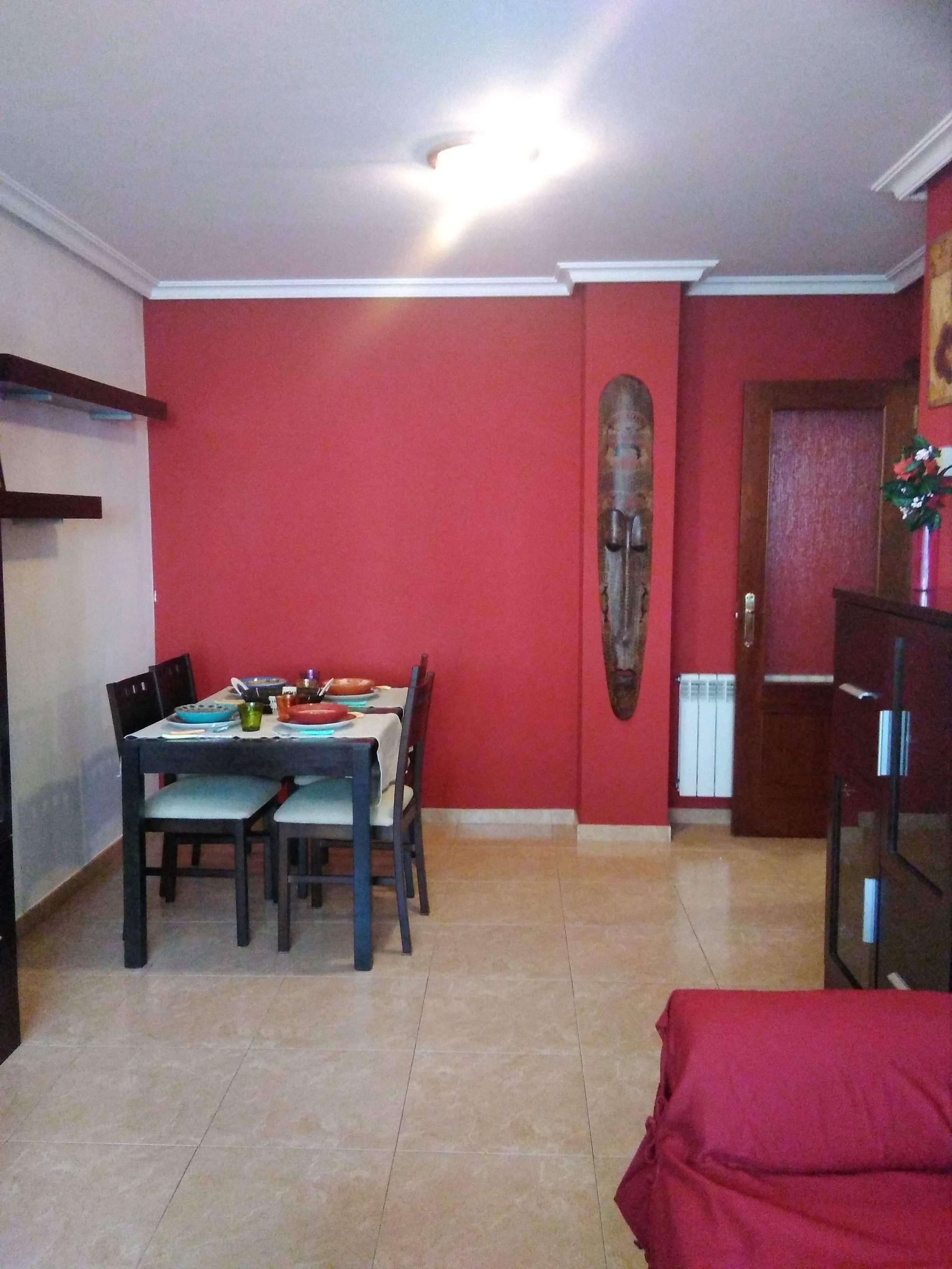 Un comedor con pared roja, una mesa de madera y sillas.