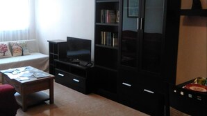 Een woonkamer met een bank, een salontafel, een tv-meubel en een zwarte kast met planken.