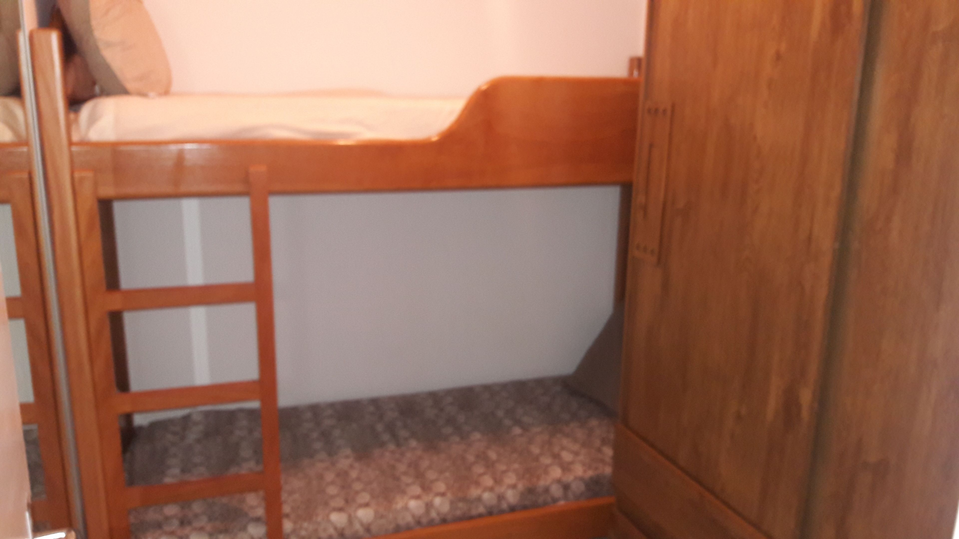 Een stapelbed met een houten ladder, een matras en een opbergkast.