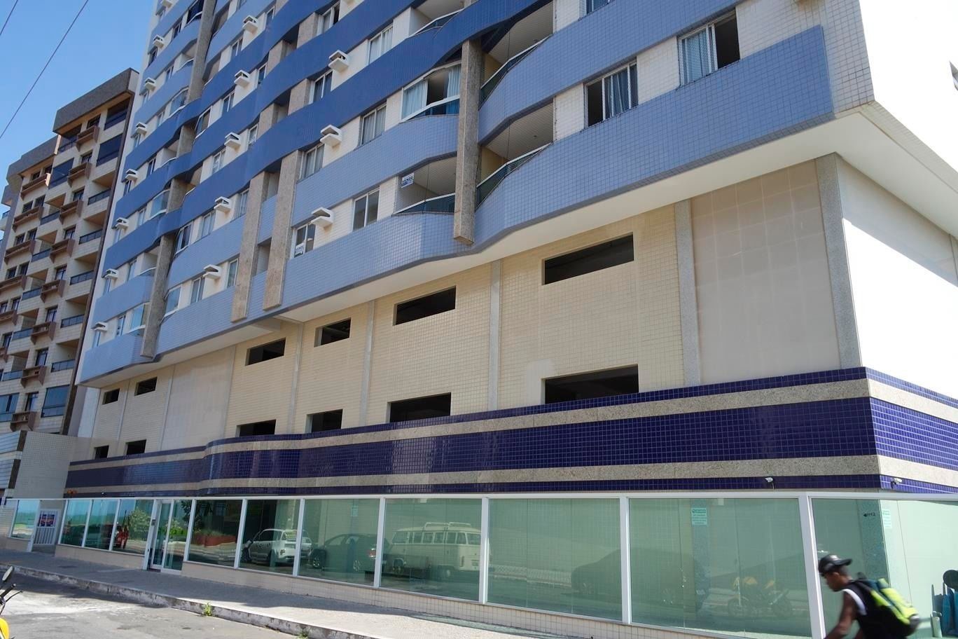 Un edificio de varios pisos con fachada plana, ventanas grandes en la planta baja y balcones en los pisos superiores.