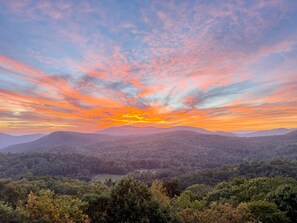 A landscape with a sunset over a forested valley and distant hills.