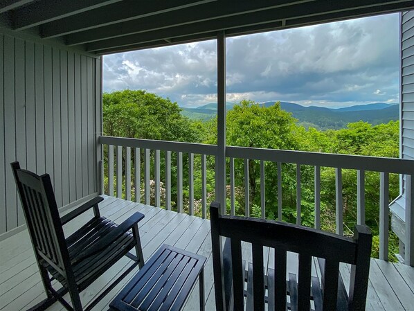A wooden deck with a white railing, two wooden chairs, and a view of a mountainous landscape with trees. - Three Private Balconies. One Panoramic Mountain View. Floor-to-Ceiling Windows | VZ Top 303 (Highlands)