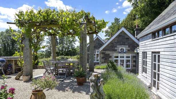 A rustic stone building with a wooden pergola, outdoor seating, and a statue. - The School House, Coryton - a peaceful retreat  (sleeps 6+toddler) (Devon)