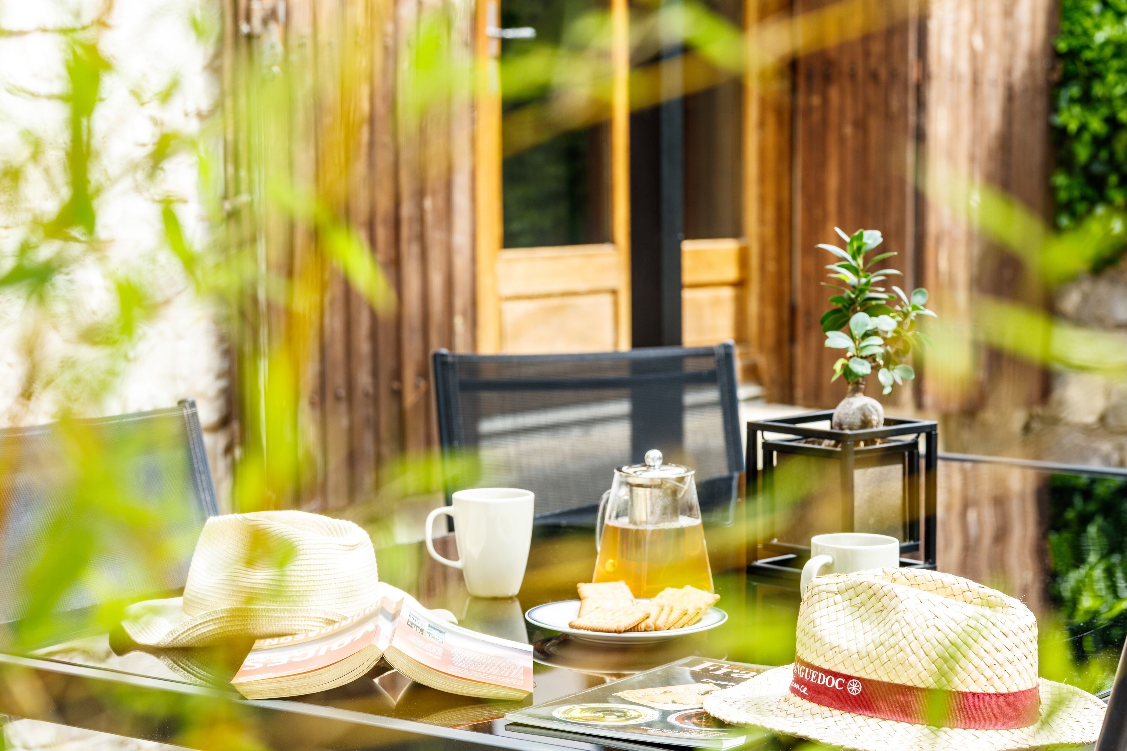 Une table dressée avec un chapeau, un livre, un verre de jus, une tasse et une théière.