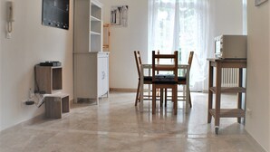 Una habitación con una mesa de comedor y sillas, un armario, un reloj en la pared y una ventana con cortinas.