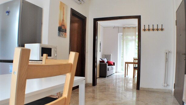 Una cocina moderna con microondas, una mesa de comedor de madera y sillas. Se ve un pasillo que conduce a una sala de estar con un sofá y una pequeña mesa.