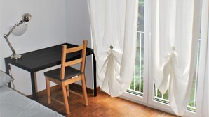 Un dormitorio con cama, escritorio, silla y ventana con cortinas.