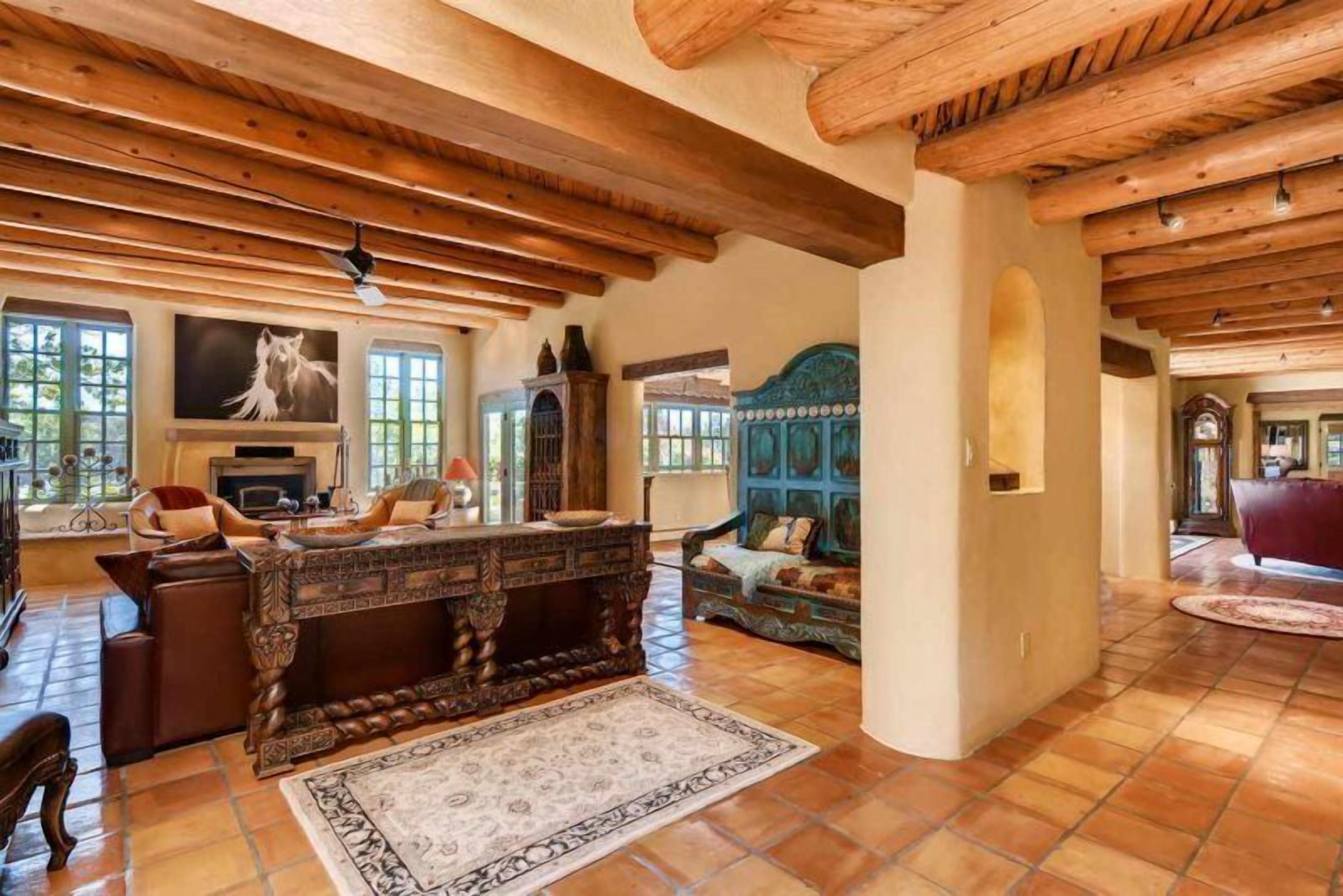 Un salon spacieux doté d’une cheminée, de poutres en bois et d’un grand tapis.
