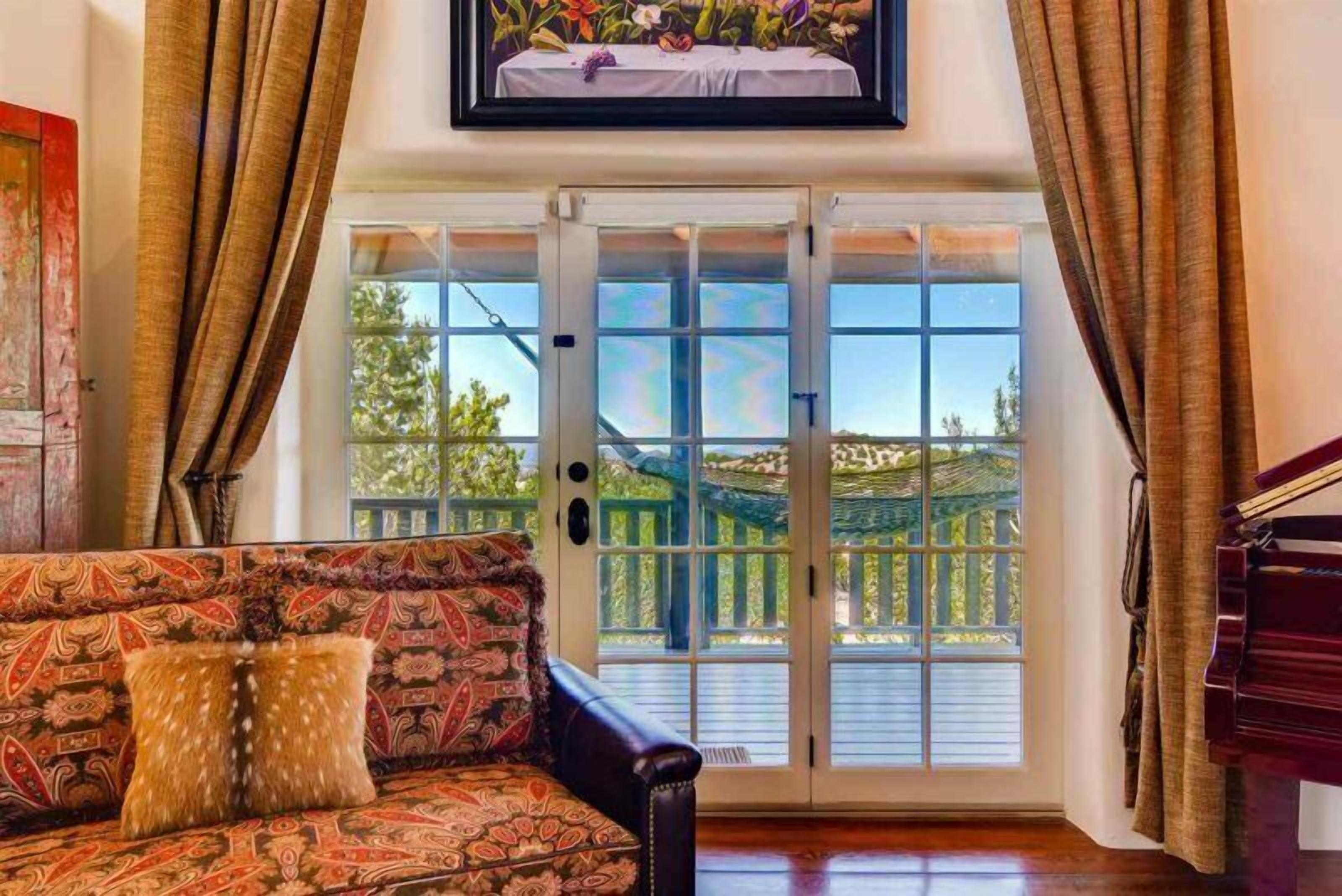 A living room with a patterned sofa, a piano, and a sliding glass door leading to a balcony.