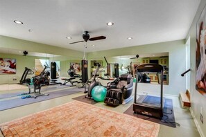 Ein geräumiger Home-Fitnessraum mit verschiedenen Trainingsgeräten, darunter ein Laufband, ein Indoor-Fahrrad und ein Rudergerät.