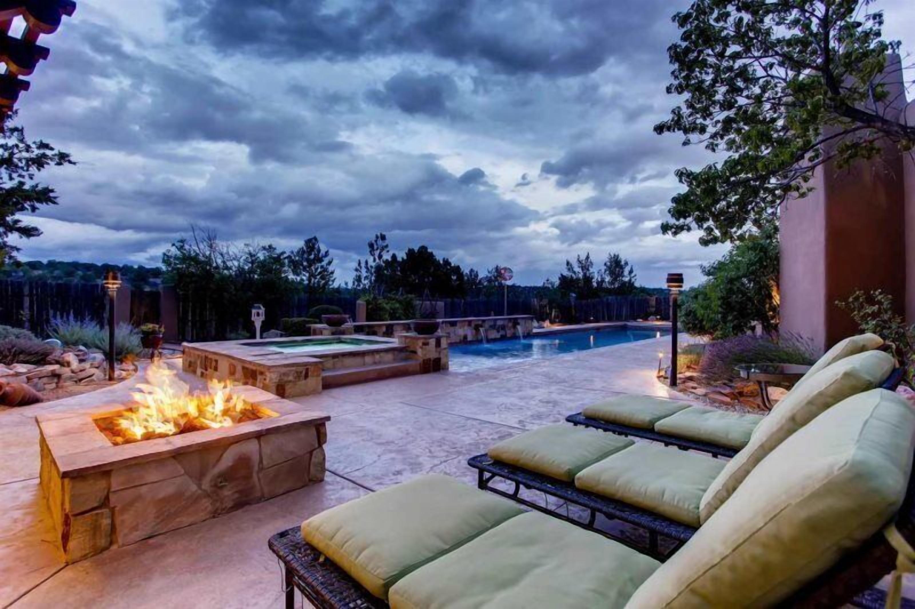Ein Garten mit Pool, Feuerstelle und Liegestühlen.