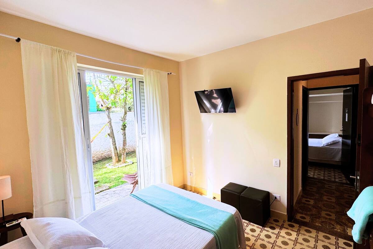 A hotel room with a bed, a TV, a desk with a lamp, and a view of the outside.