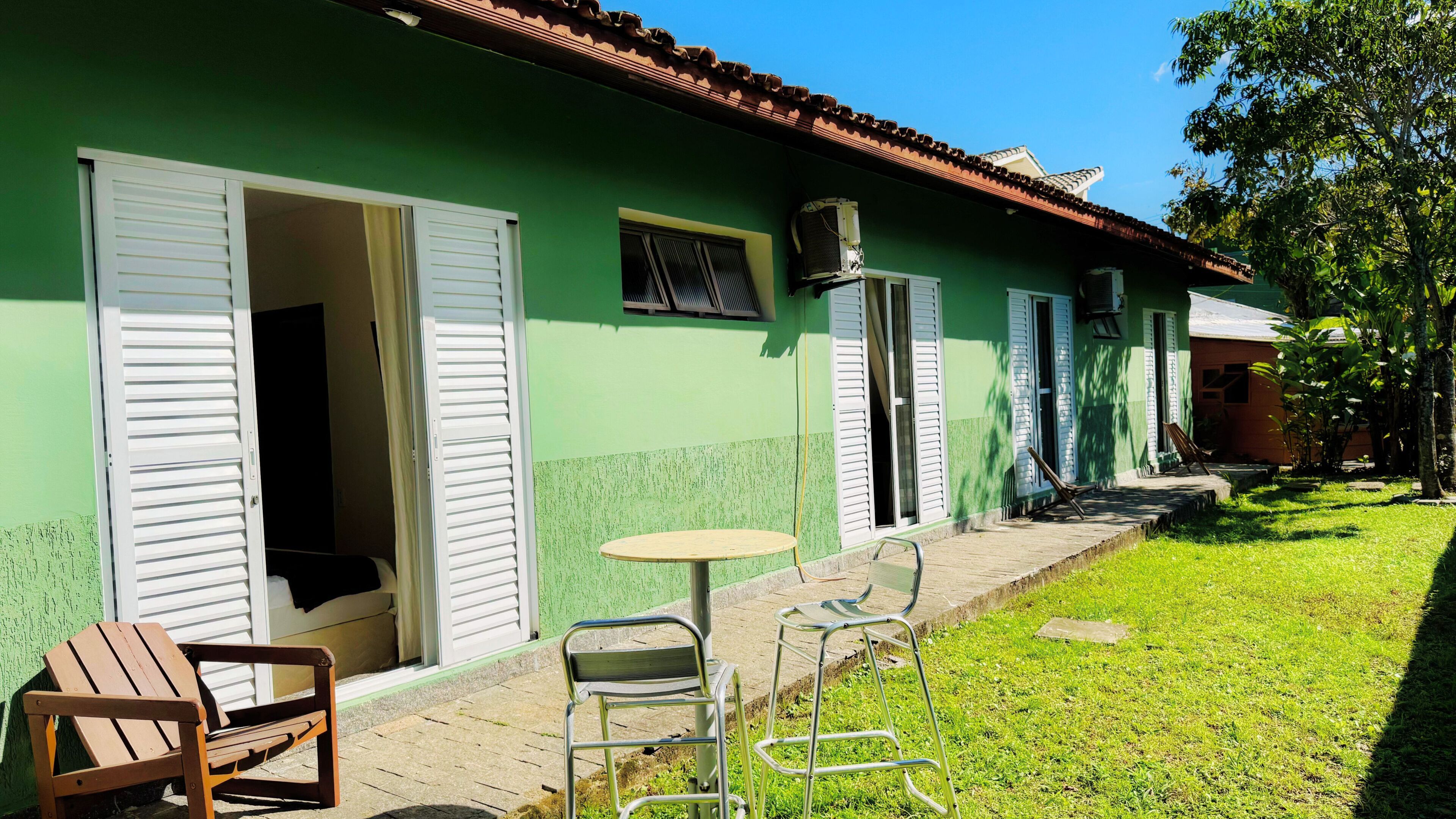 A green building with white shutters, a small patio with a round table and metal chairs, and a grassy lawn.