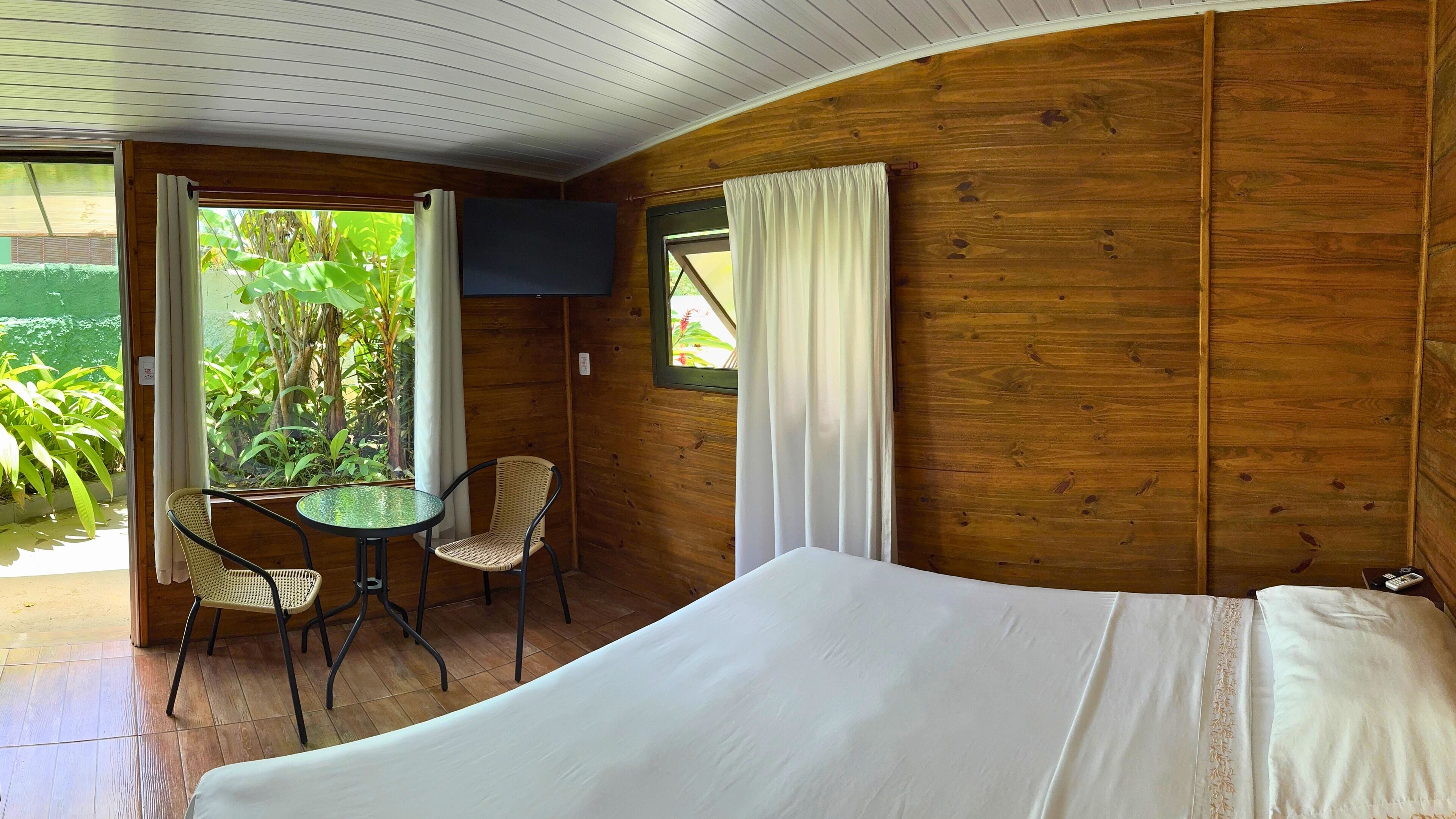 A wooden room with a bed, a small table, two chairs, and a TV on the wall.