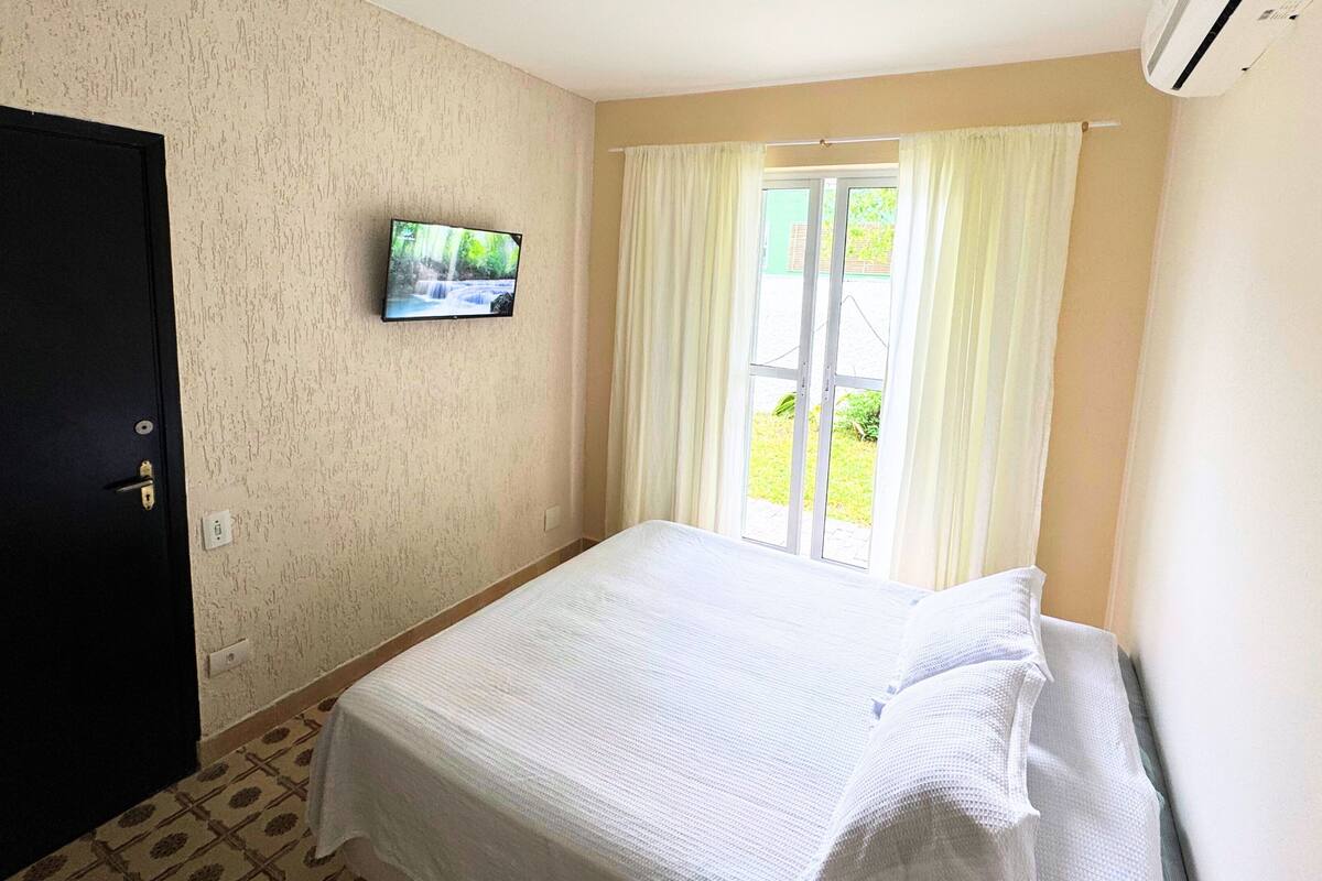 A bedroom with a bed, a television on the wall, and a window with curtains.