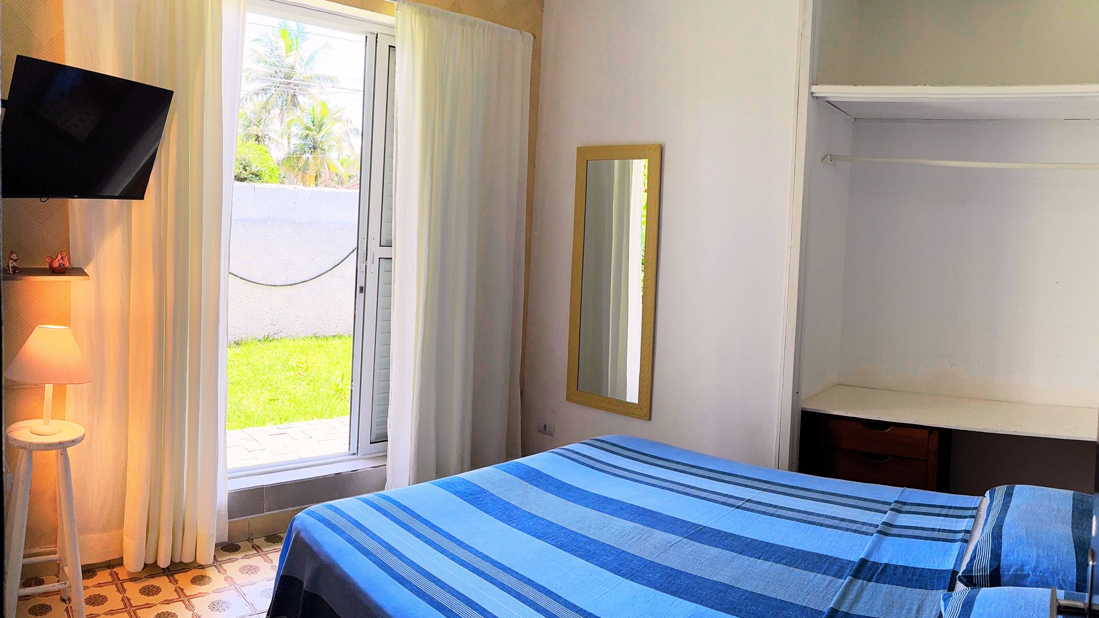 A hotel room with a bed, a television on the wall, a window with curtains, and a lamp.