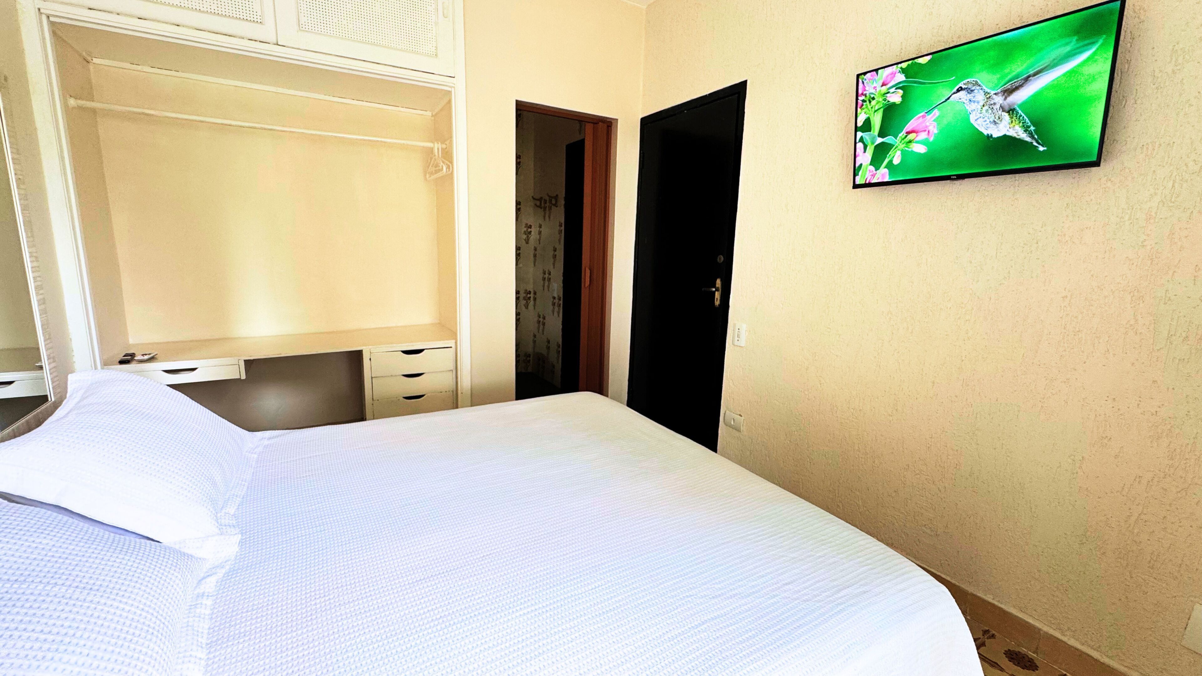 A hotel room with a bed, a wardrobe, a television on the wall, and a door.