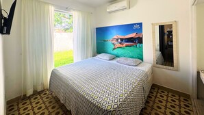 Ein Hotelzimmer mit Bett, einem fensterbelaubten Fenster, einer Wand-Klimaanlage und einem großen Poster mit Strandmotiv.