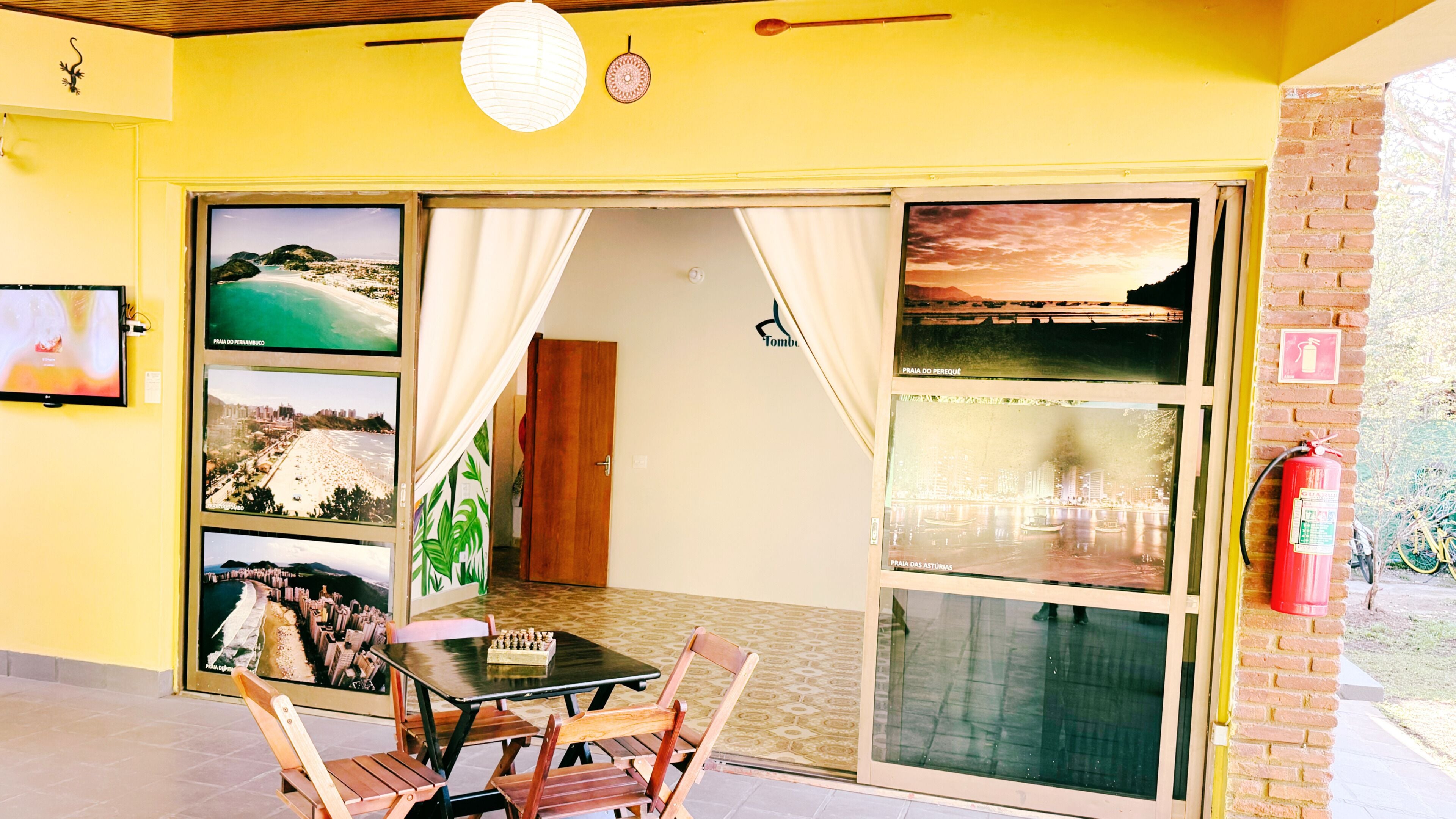 Quarto com mesa e cadeiras, televisão e uma grande janela com vista para várias praias.