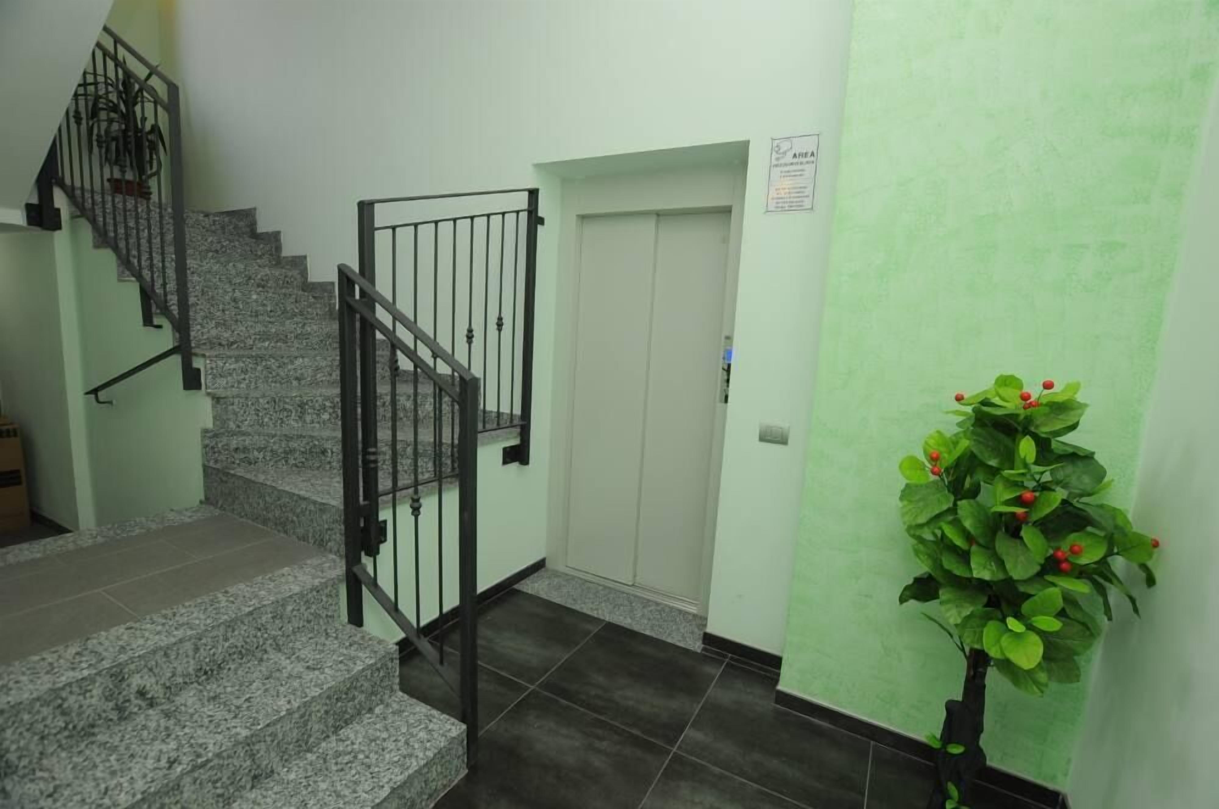 Una escalera con barandilla metálica que lleva a una puerta, una planta en maceta y una pared con un cartel.