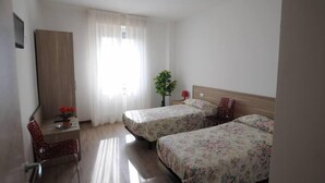 A hotel room with two single beds, a desk with a chair, a small table with a potted plant, and a window with curtains. - Comfortable Apartment in a Residence Code CIR 015209-CIM 00116 (Sesto San Giovanni)