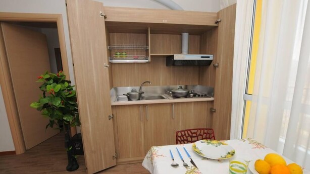 A compact kitchen with a sink, stove, and cabinets. There's a dining table with plates and a potted plant. - Comfortable Apartment in a Residence Code CIR 015209-CIM 00116 (Sesto San Giovanni)