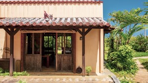 A traditional building with a tiled roof, wooden porch, and a small statue. - Somos (Nakijin)