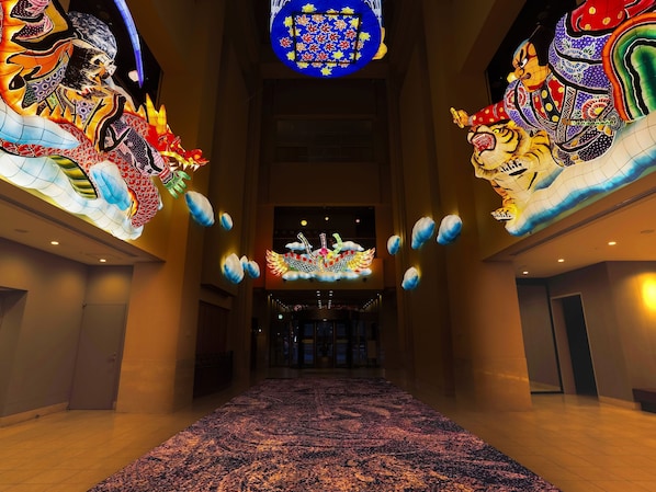 A hotel lobby with a large, ornate chandelier, a patterned carpet, and a view of the entrance.