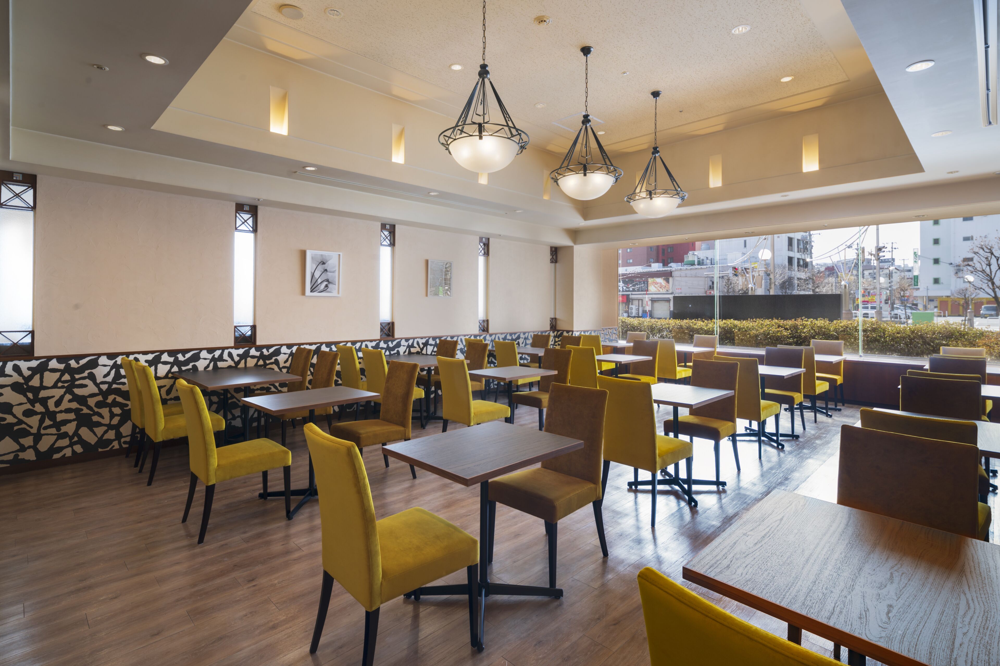 A spacious dining area with yellow chairs and wooden tables, large windows offering a view of the city, and pendant lighting.