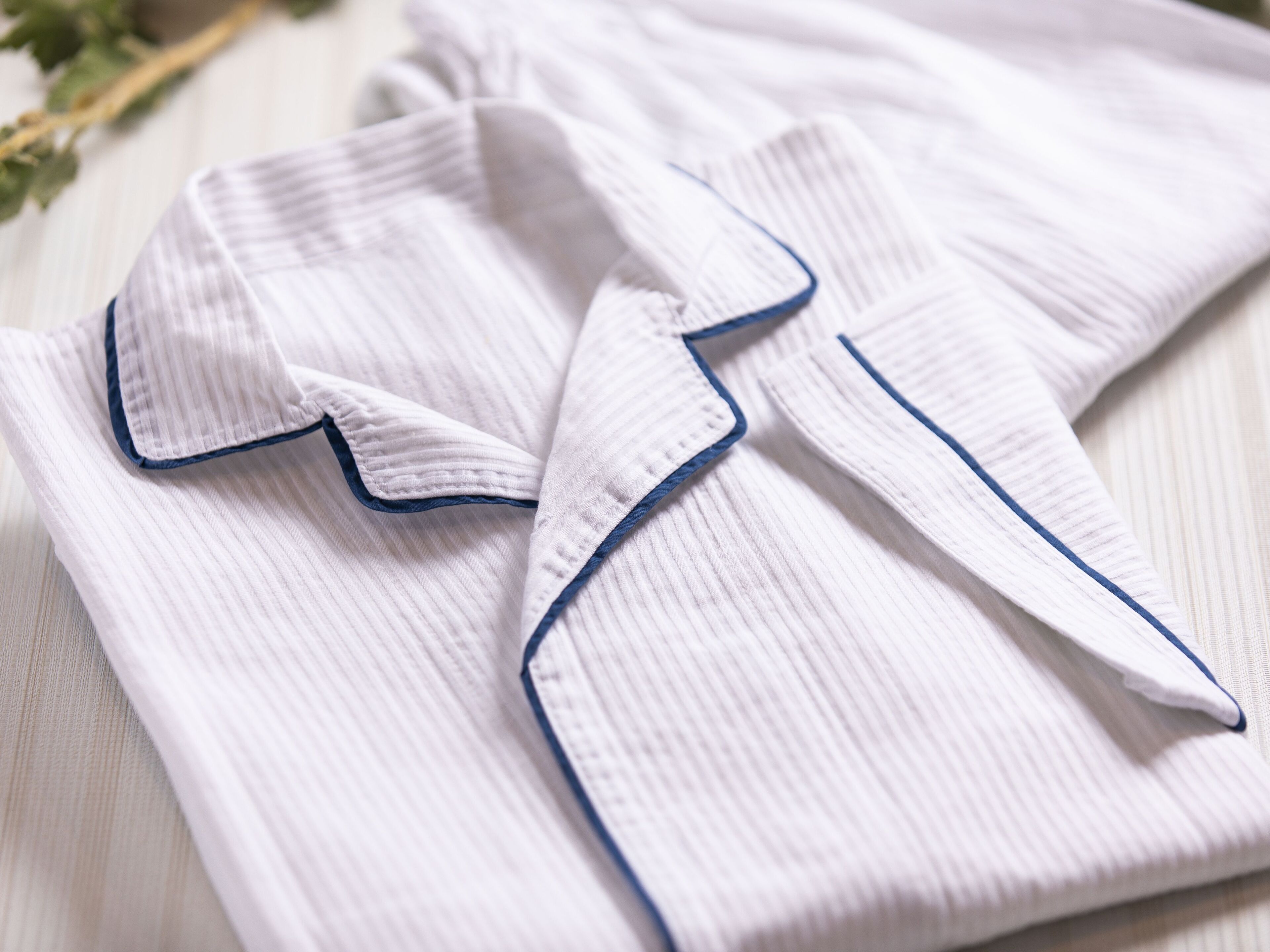 A neatly folded white shirt with blue piping on a wooden surface.