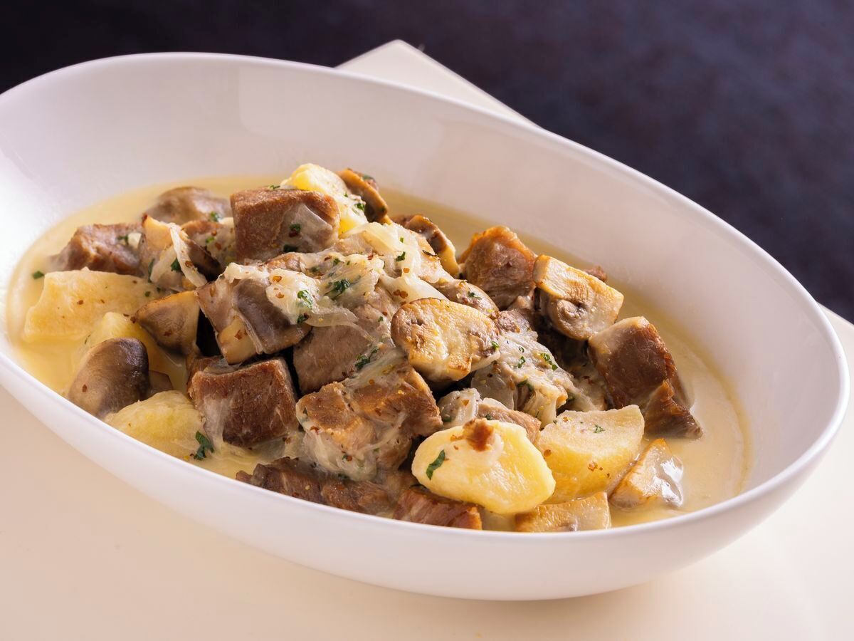 A white oval dish containing a stew with chunks of meat and potatoes, garnished with herbs.