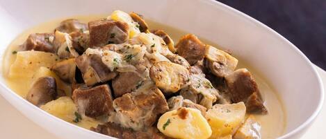 A white oval dish containing a stew with chunks of meat and potatoes, garnished with herbs.