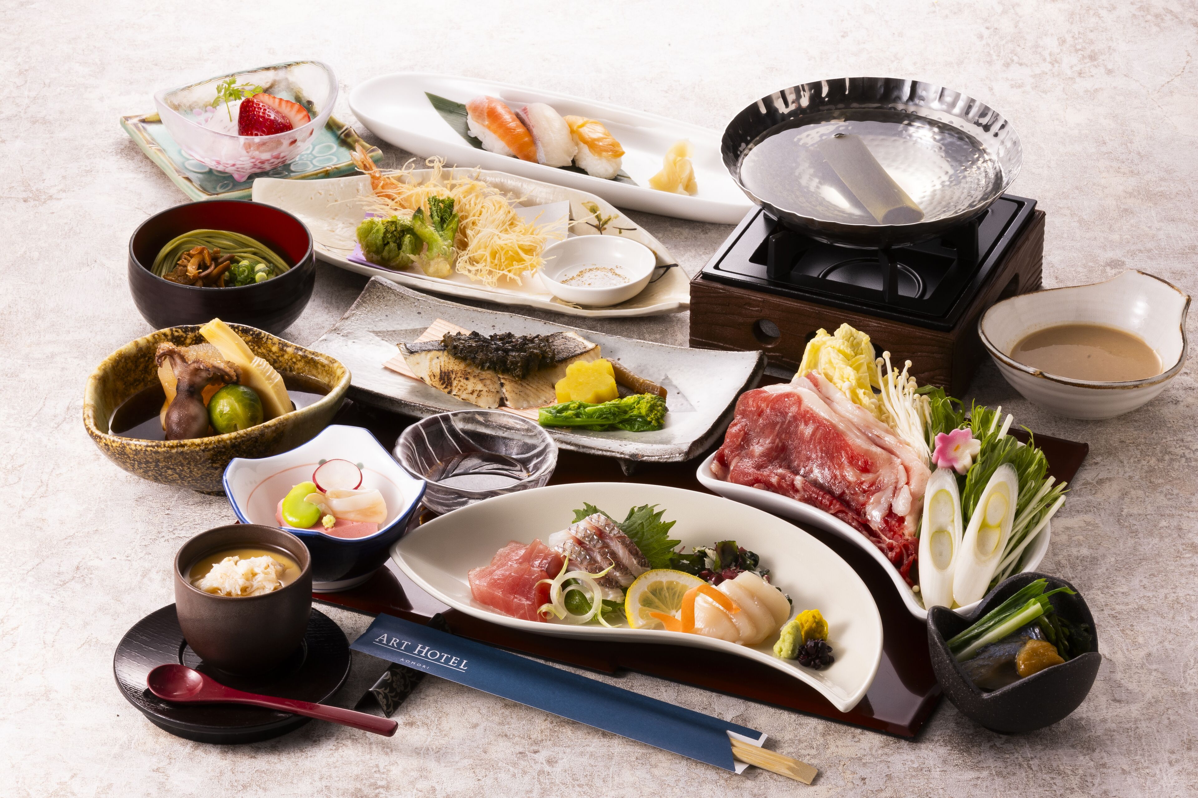 Verschiedene japanische Gerichte, darunter Sushi, Sashimi und Gemüse, angerichtet auf einem Tisch mit Teekanne und Stäbchen.