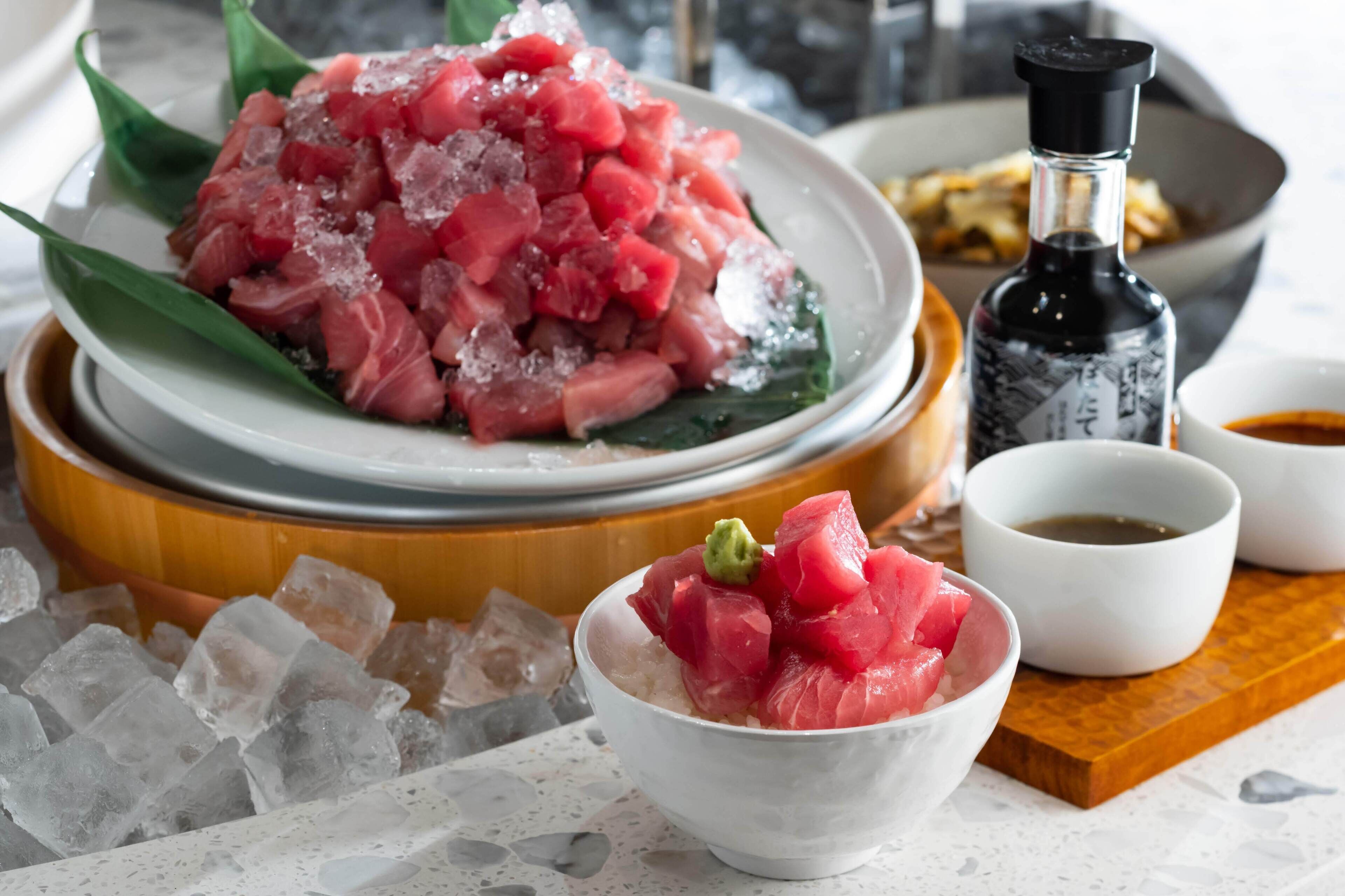 A bowl of raw fish on a wooden plate, ice cubes, and two small bowls of soy sauce.