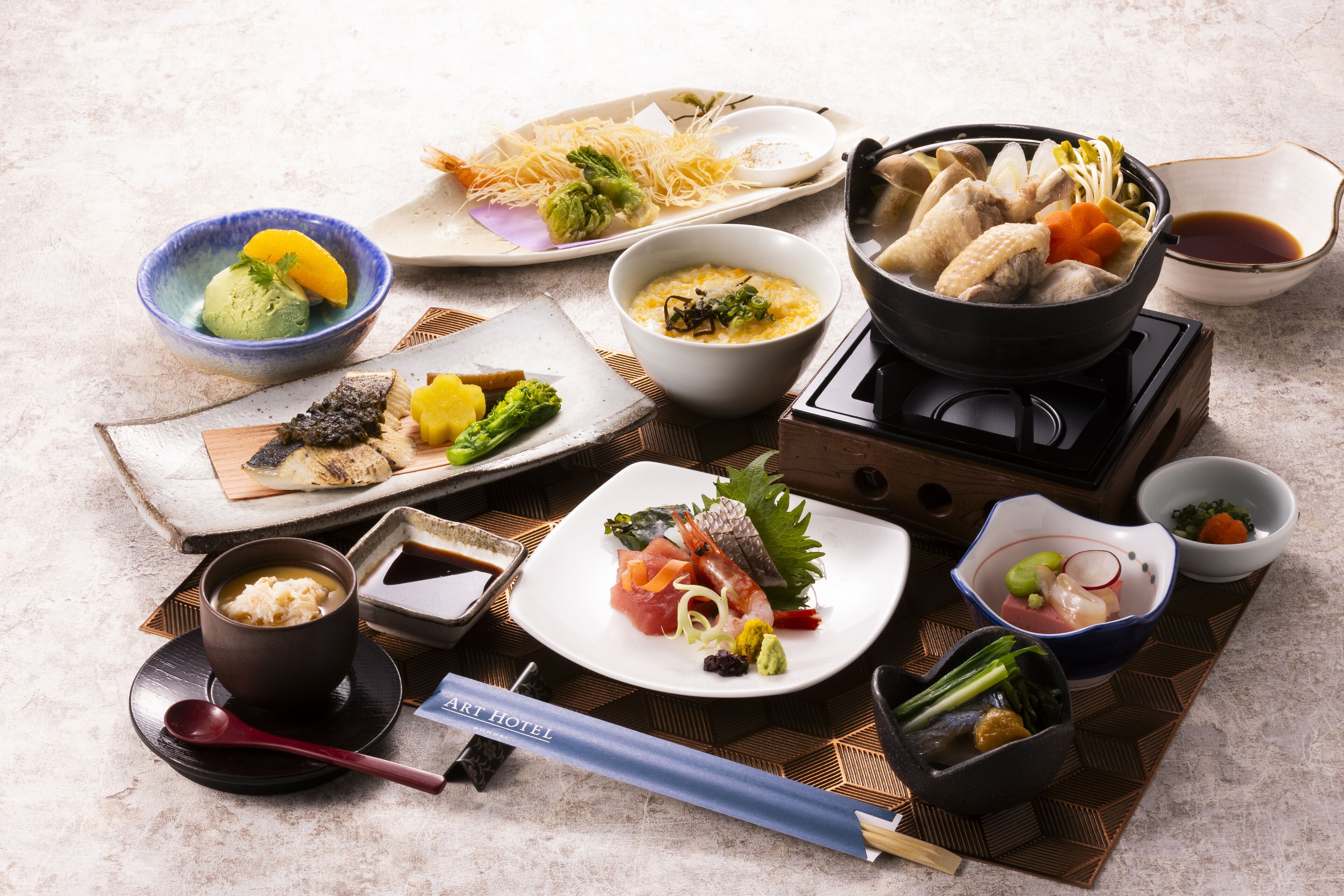 A variety of Japanese dishes including sushi, sashimi, and a hot pot, arranged on a table with chopsticks and bowls.