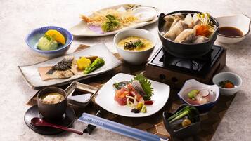 A variety of Japanese dishes including sushi, sashimi, and a hot pot, arranged on a table with chopsticks and bowls.